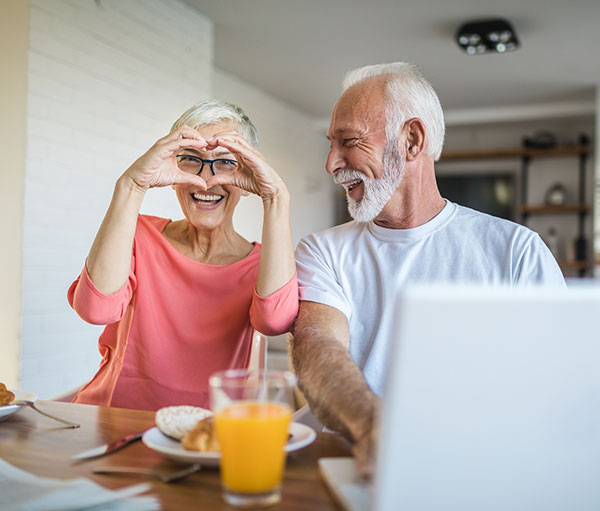 senior couple sitting at computer - woman has hands in the shape of a heart