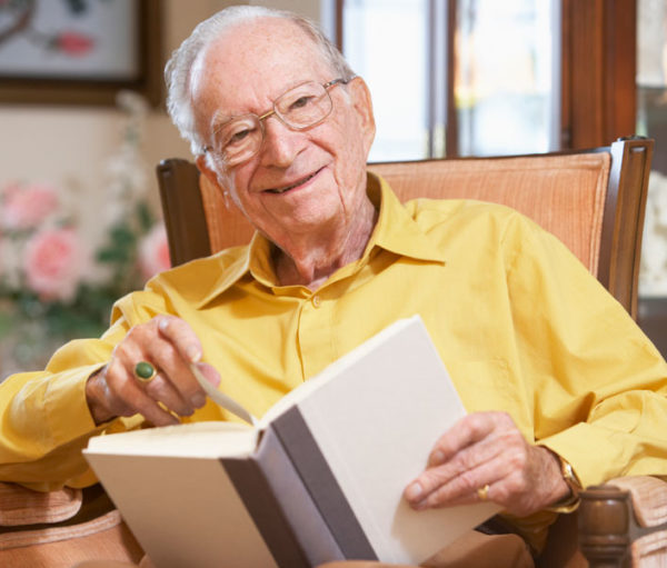 Elderly gentleman smiling and reading a book.