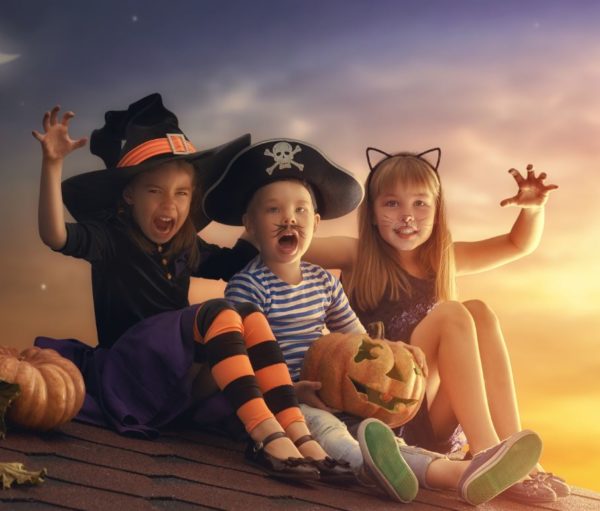 three children dressed in Halloween costumes sitting on roof of house